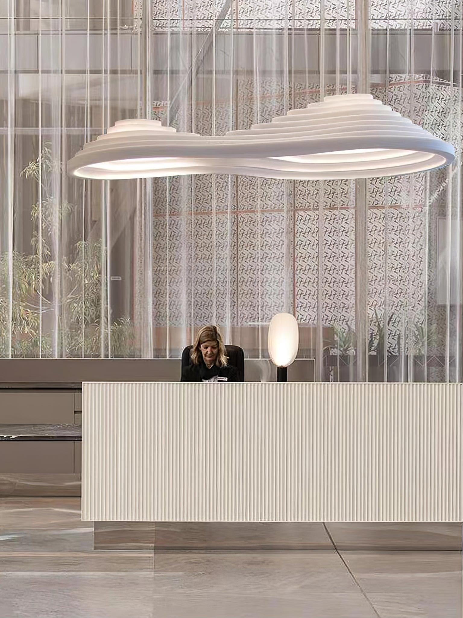 Elongated contoured pendant above a ribbed white reception desk and sheer curtains.