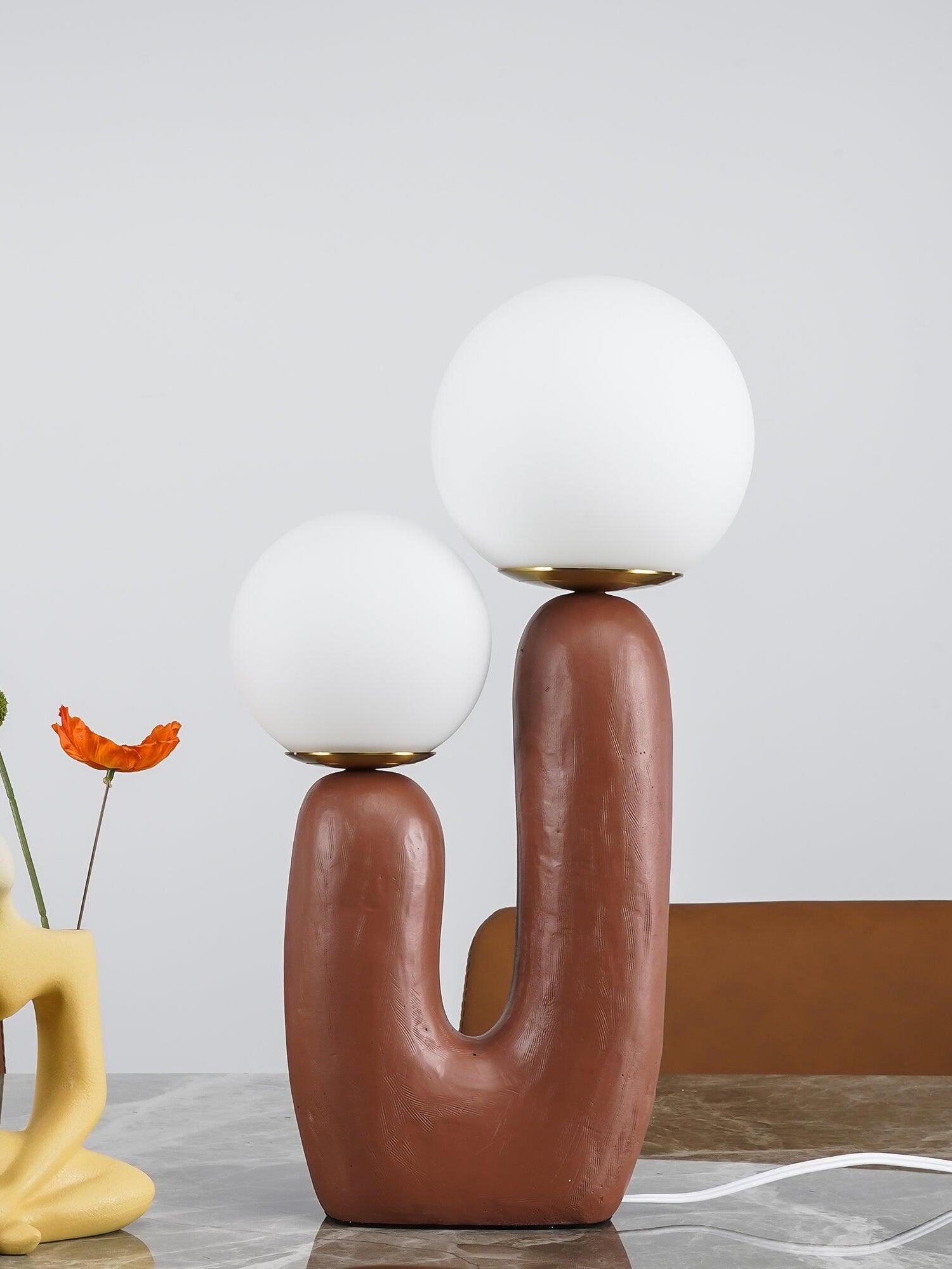 Terracotta Oo Rough lamp with two opal globes on marble beside a yellow flower vase, with a brown chair behind