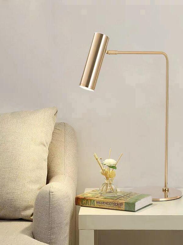 Gold-tone lamp with angled head on side table beside armchair, books and flower