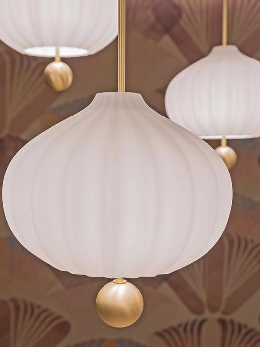 Lilli shade and brass ball in close-up, with two other white fluted pendants against a floral background