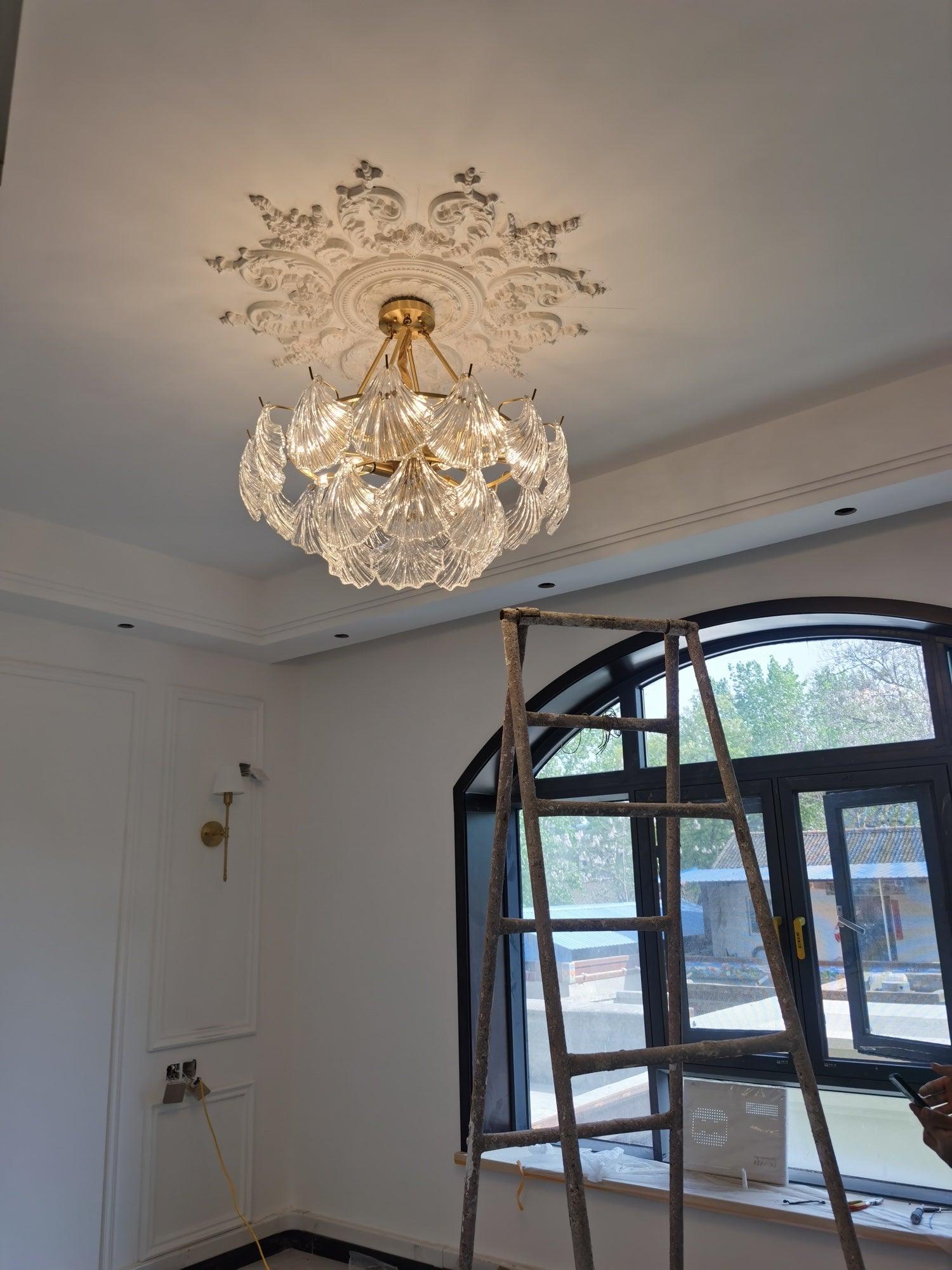 Shell-panel fixture beneath an ornate ceiling medallion near an arched window and ladder