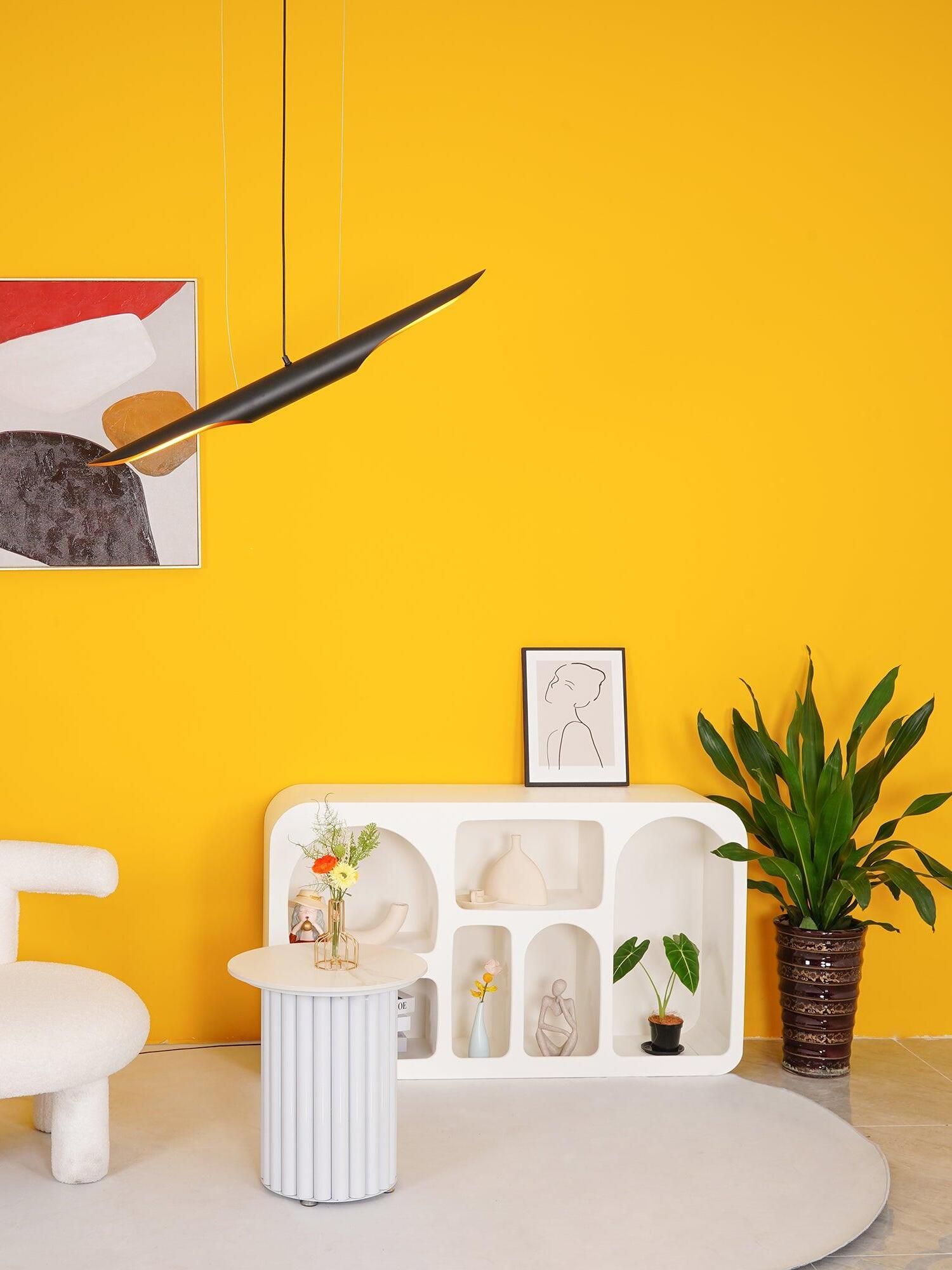 Tilted pipe pendant above a flower table and white shelf beside a large plant on a yellow wall
