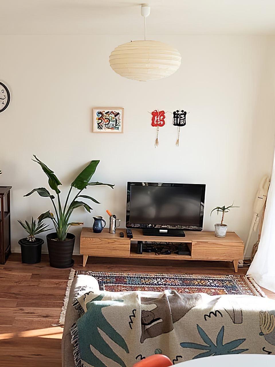 White paper lantern above a living-room TV and wooden console, with leafy plants, wall decorations and patterned sofa