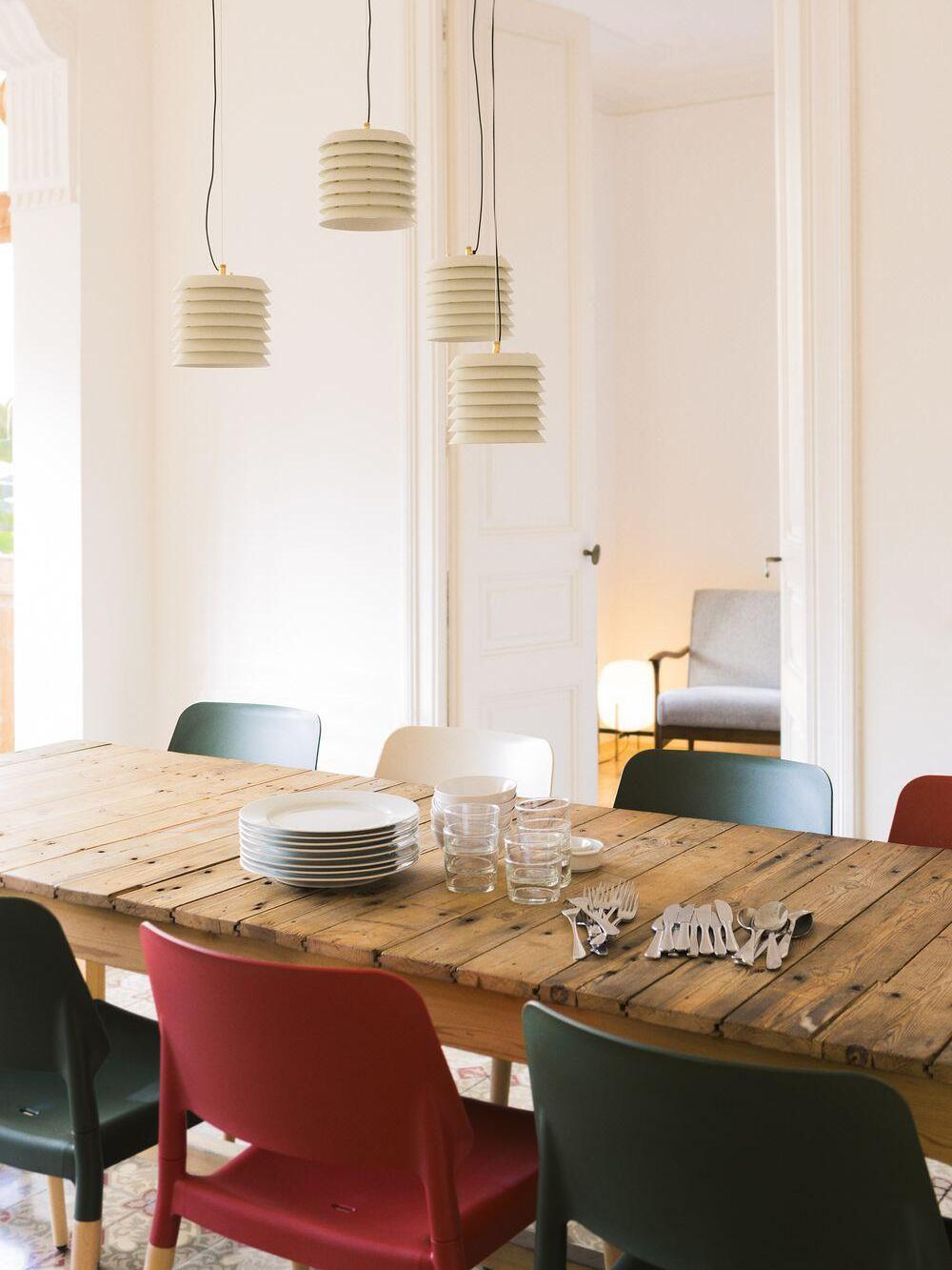 Four pale layered pendants above wood table with plates and colourful chairs