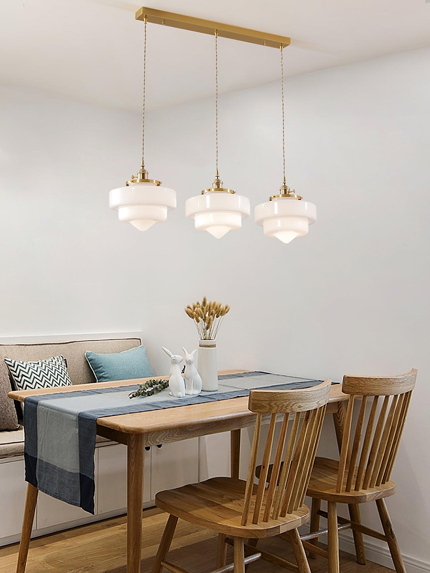 Atlas Model A three-head pendant with shared brass canopy above a wooden table, blue-gray runner and patterned cushions