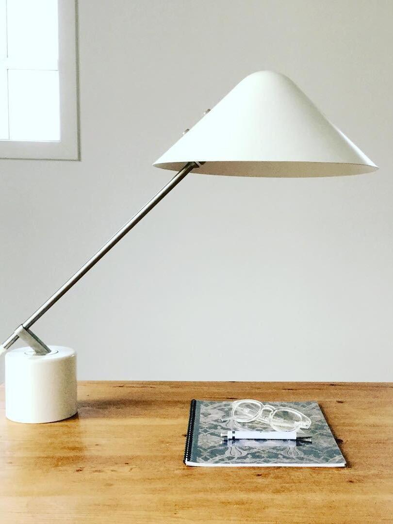 White shade and silver-tone diagonal arm above a wood table with a magazine