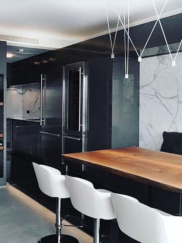 White geometric light arrangement above a wooden kitchen counter with white stools and dark cabinets