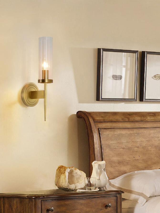 Glass wall sconce beside a wooden headboard