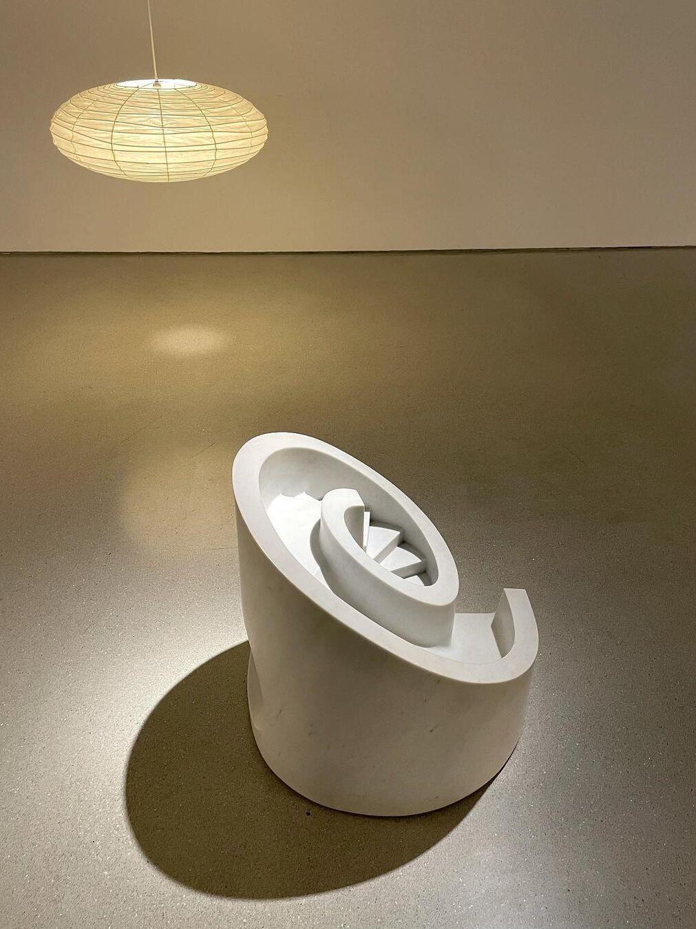 Flattened illuminated paper lantern above a large white spiral sculpture in an exhibition space
