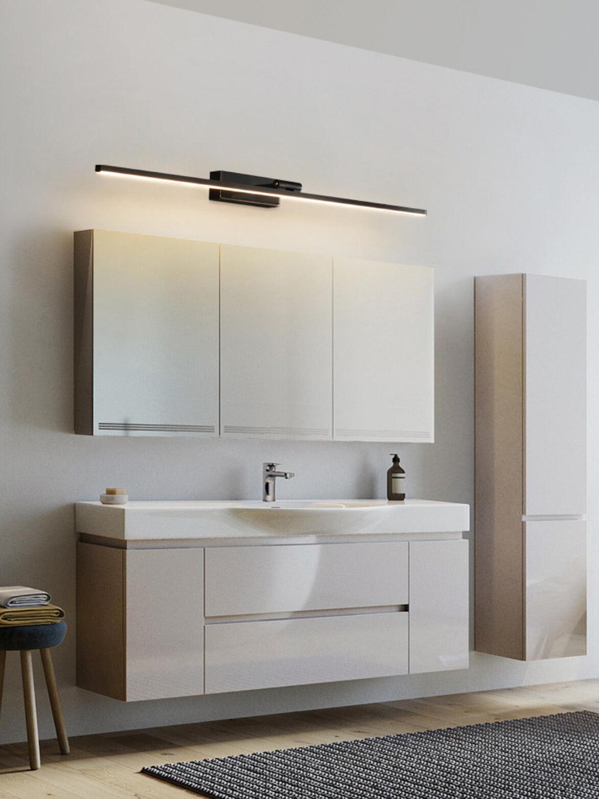 Black linear wall light above three-panel mirror cabinet, white basin, faucet and soap beside tall cupboard