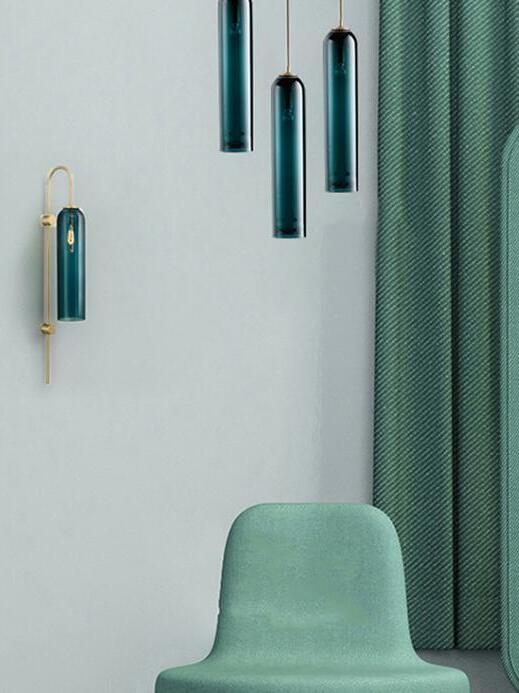 Three blue-green tube pendants at staggered heights above a green chair, with a separate wall lamp at the left