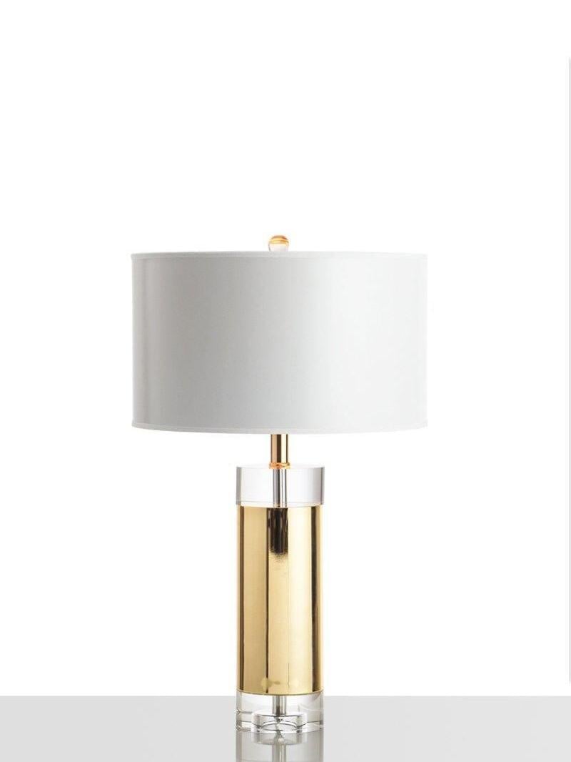 Isolated white-shade gold-tone cylinder lamp with clear collar and base in wider crop