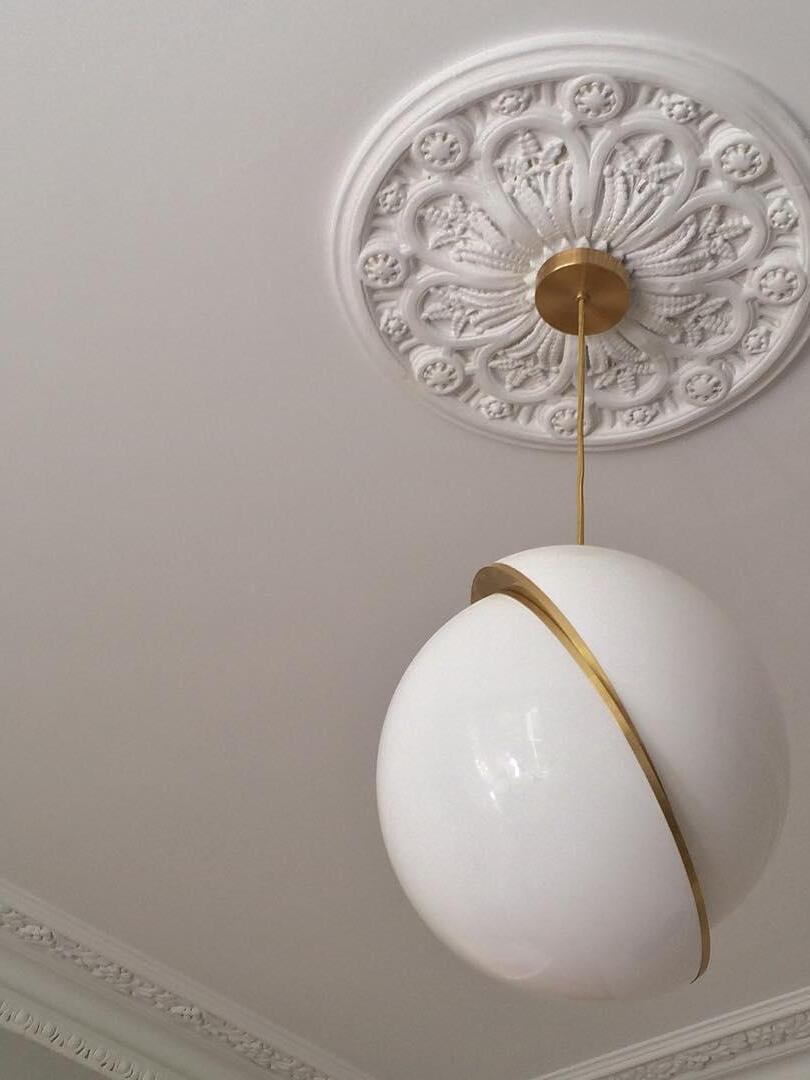 Unlit Crescent white globe pendant with a gold-colour band, cord and round canopy below an ornate ceiling rosette