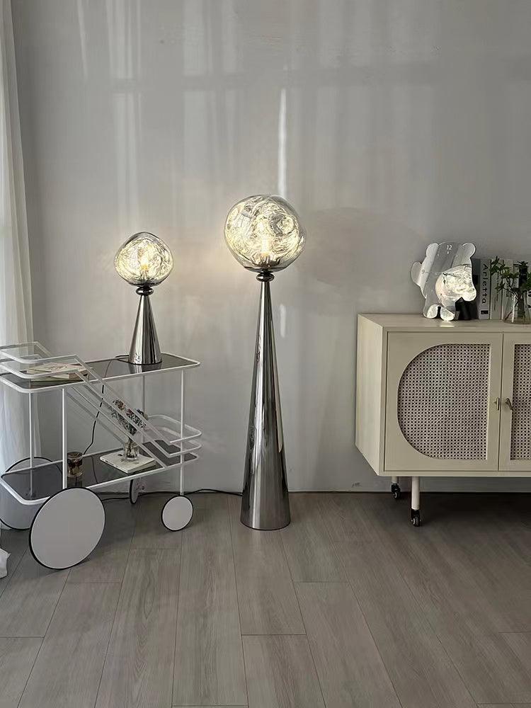 Wide view of glowing chrome table and floor lamps beside a white cart and cabinet