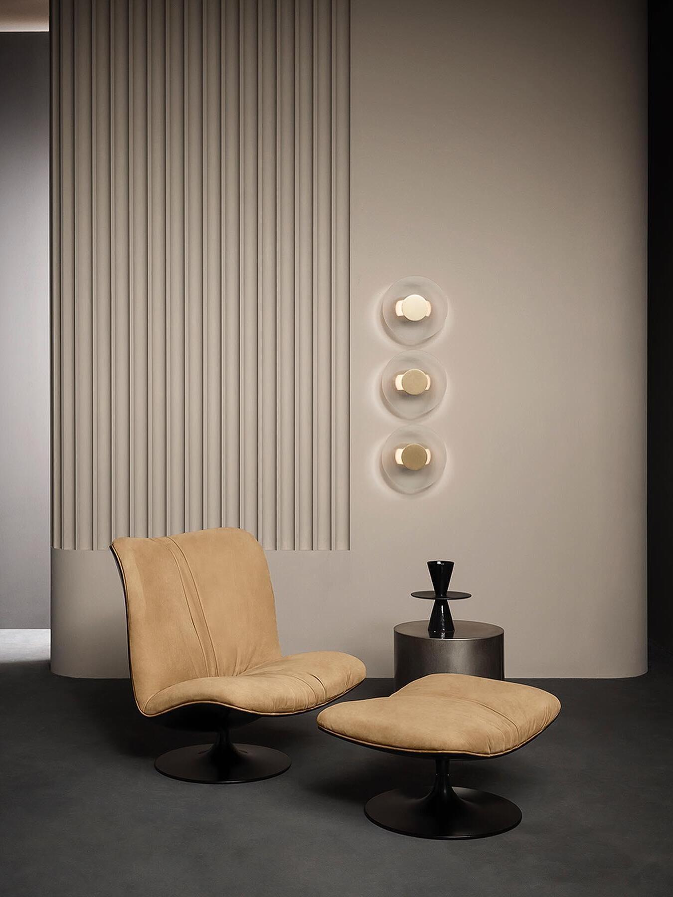 Three round Button wall lights over a tan lounge chair and footstool beside a dark cylindrical table