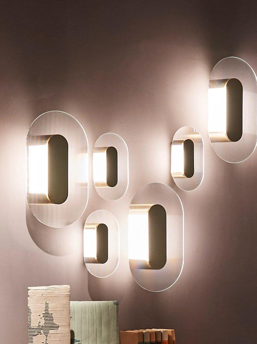 Oblique view of six lit elongated Button wall lights above leaning decorative boards on a brown wall