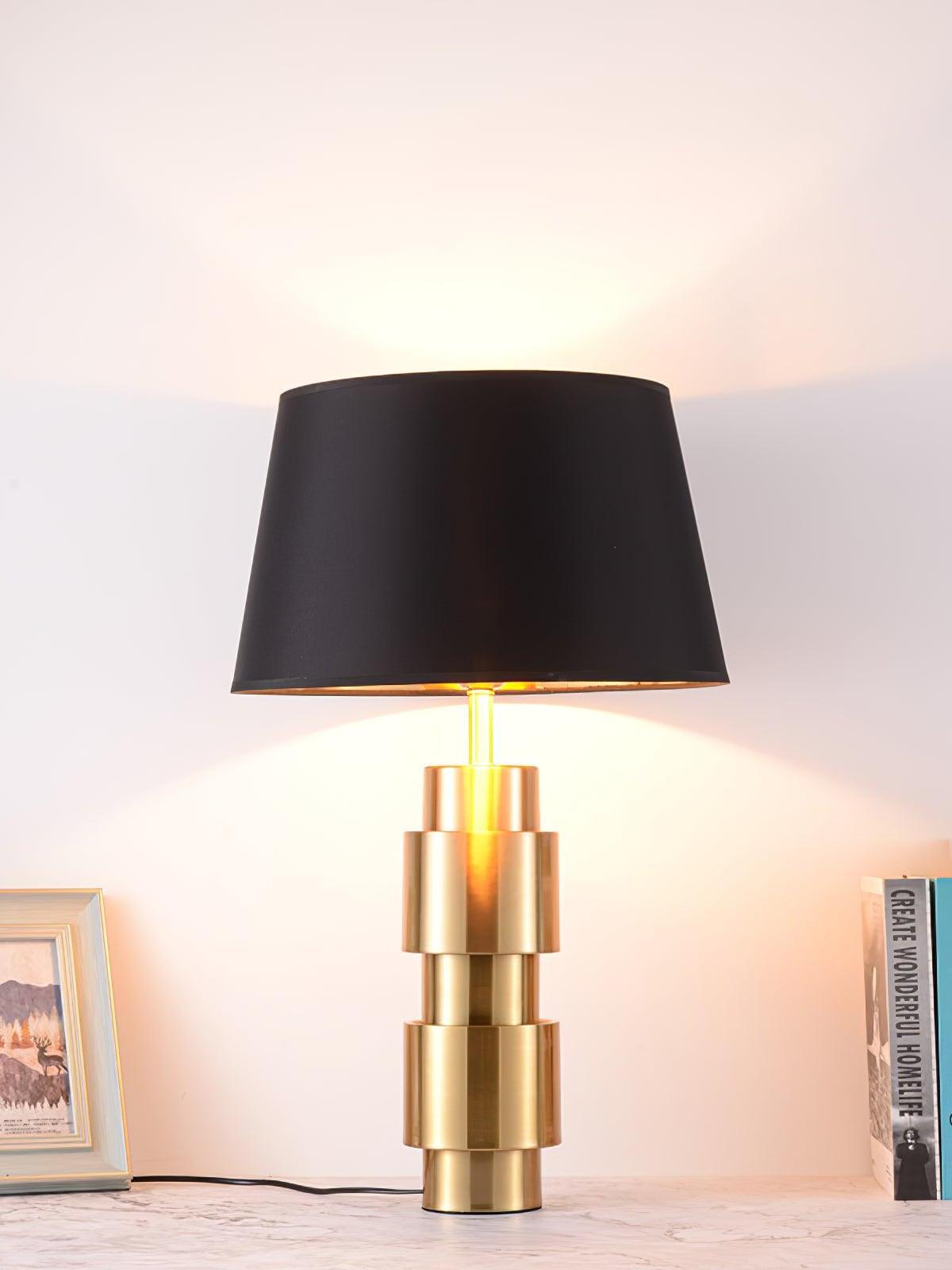 Lit Jean table lamp casting light above and below its black shade beside books and a framed photo