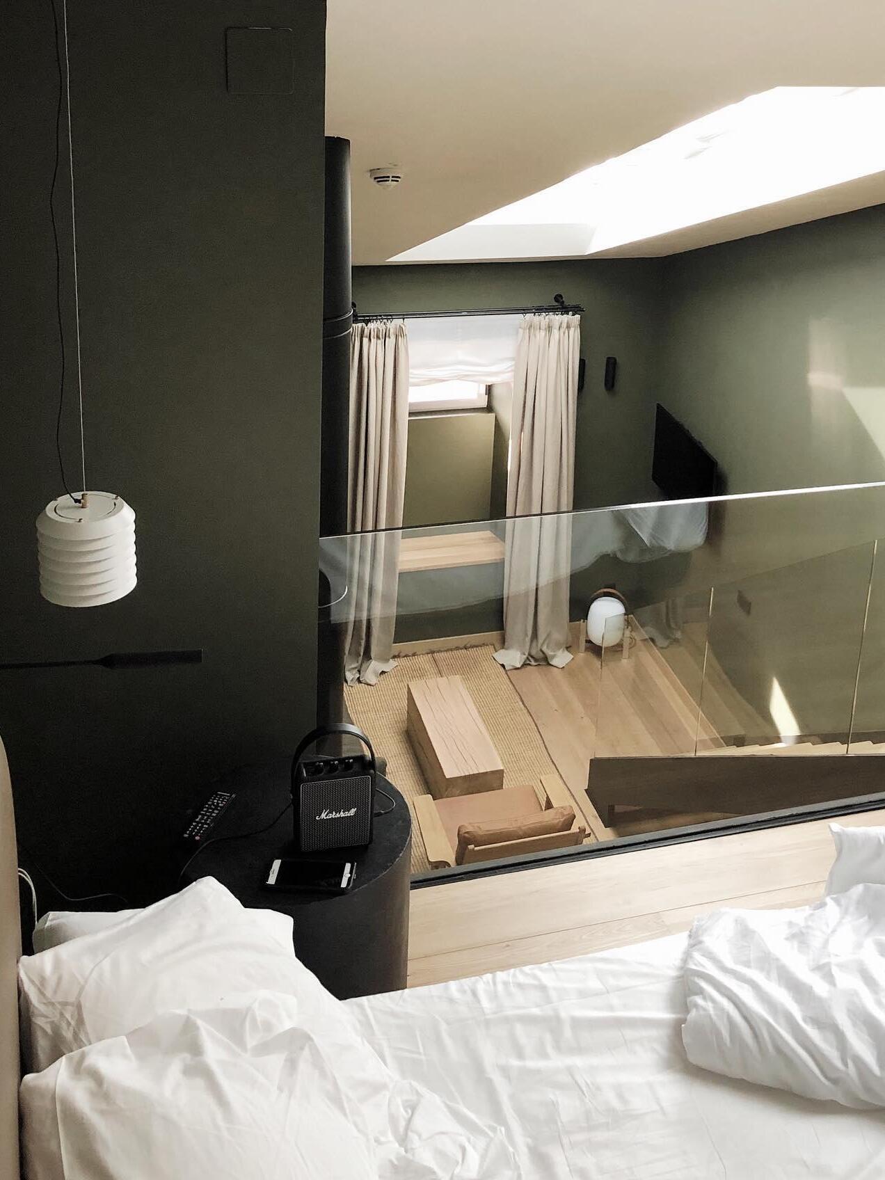 Small white pendant beside bed in dark-walled room with curtains and glazing