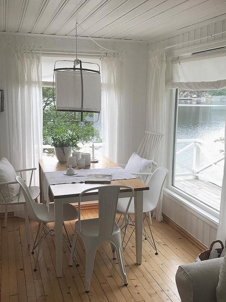White fabric bamboo pendant over wooden dining table and white chairs by large windows overlooking water