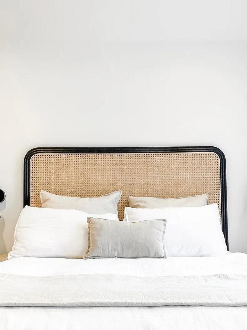 Bed and woven headboard with dark wall light partly cropped at left