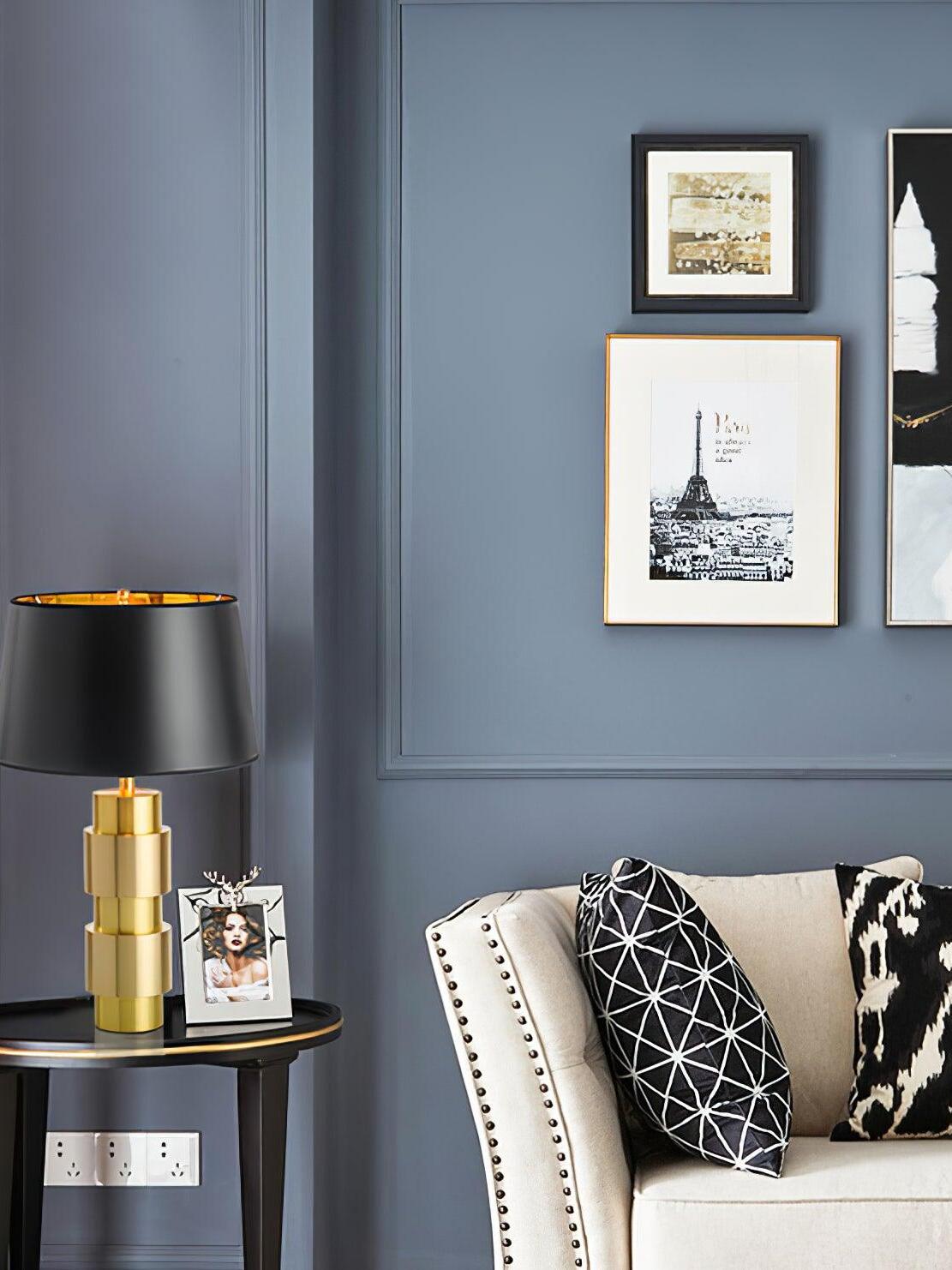 Jean lamp on a small side table in a blue room with framed art and an upholstered chair