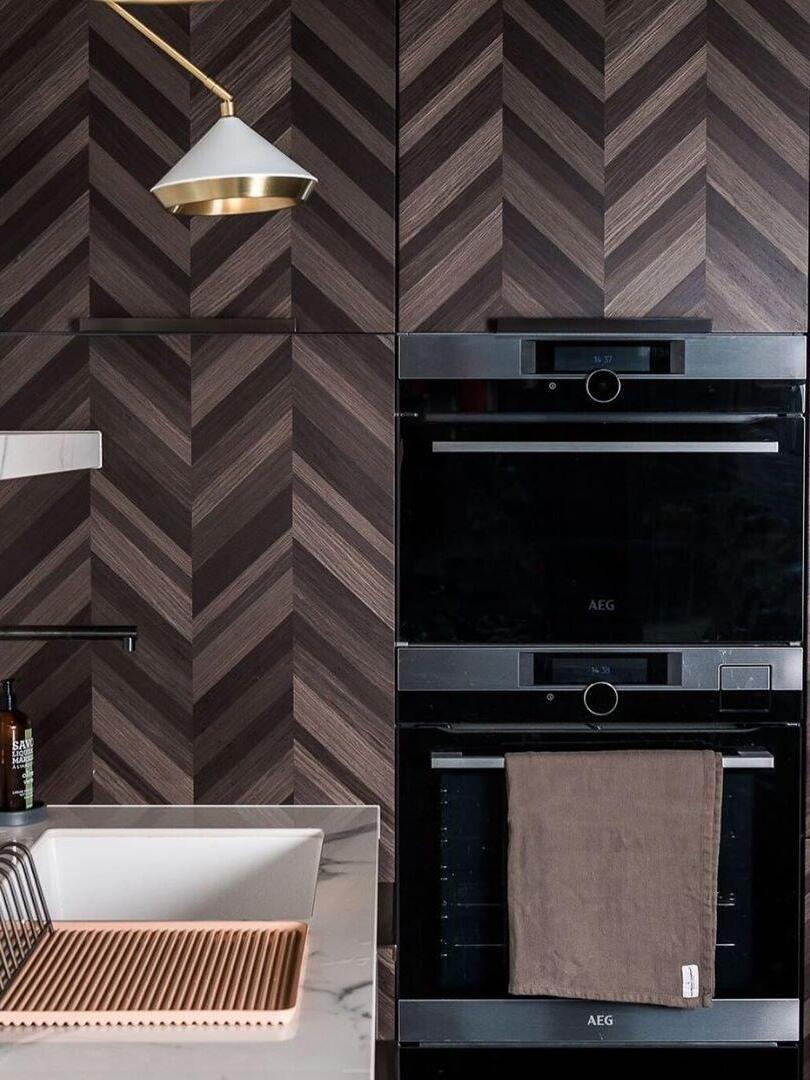 White cone shade with metallic rim above a kitchen sink beside a chevron wall and black ovens