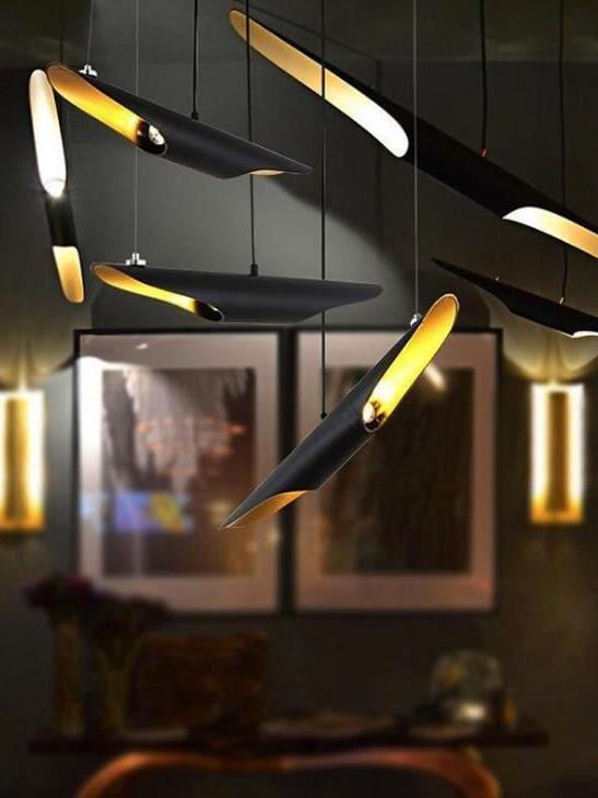 Angled black pipe pendants with illuminated gold-tone openings above framed art in a dark room
