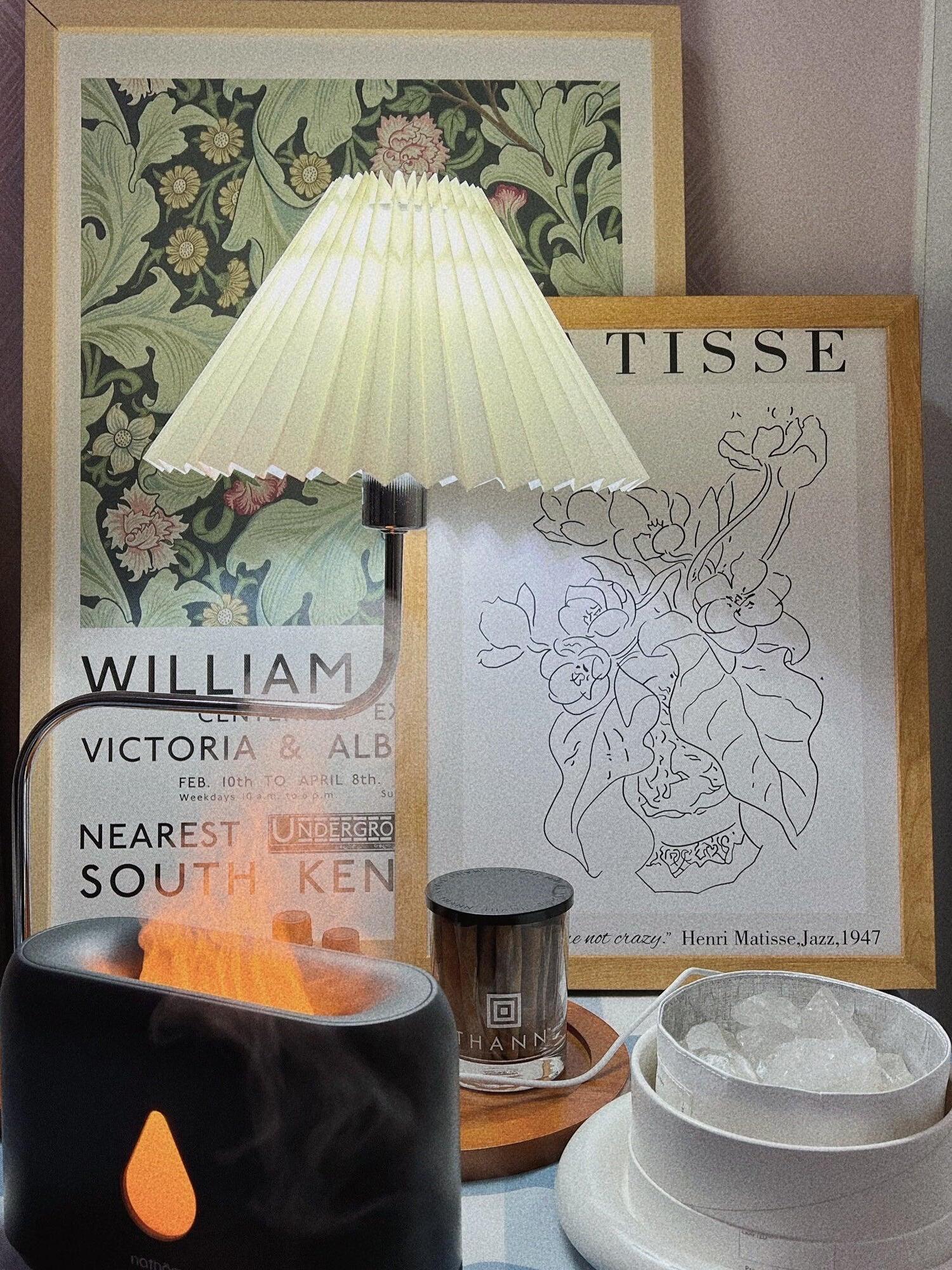 Pleated table lamp beside framed artwork