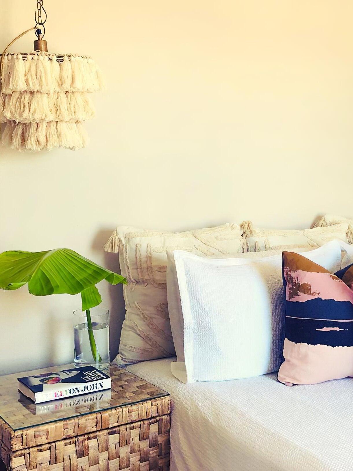 Cream tassel wall light beside a bed with white and dark cushions