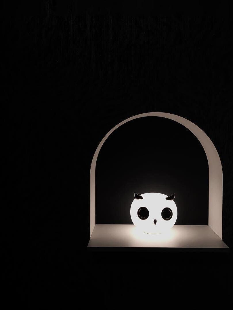 Single glowing owl lamp inside arch against dark background
