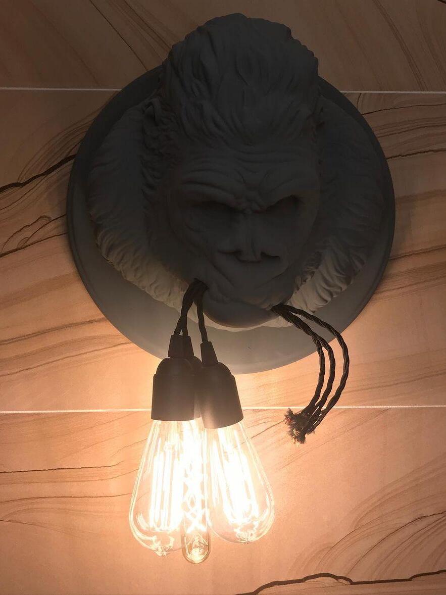 Dark gorilla head on wood panel with three glowing elongated bulbs