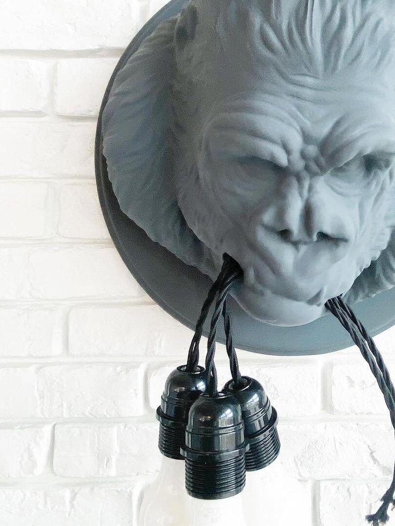 Grey gorilla relief on white brick wall with three empty bulb holders