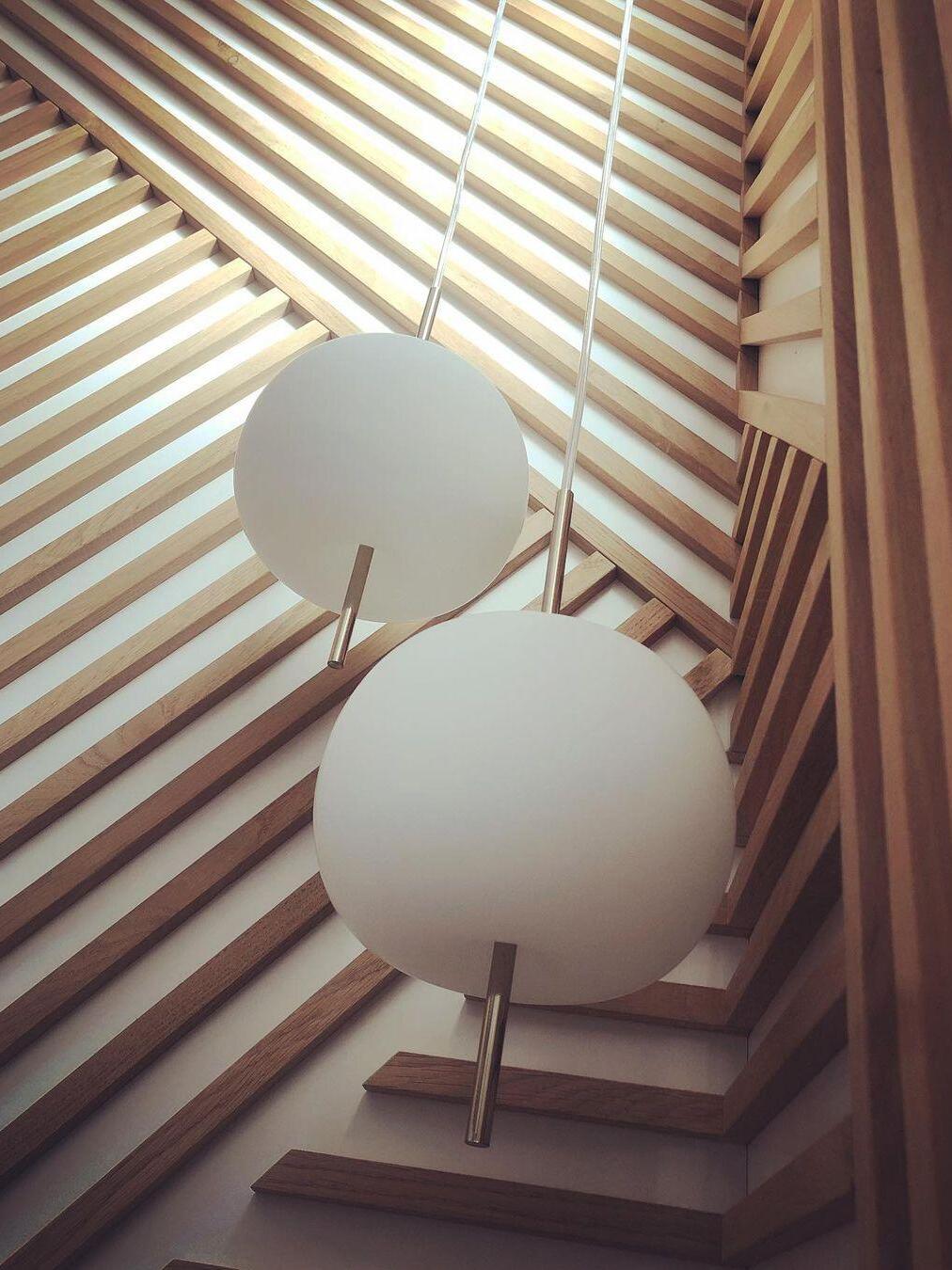 Gallery view of white rounded table-lamp forms beside slatted blinds