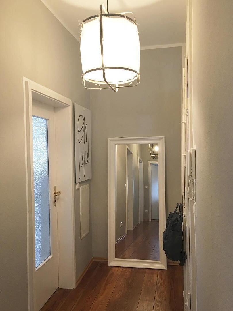 White bamboo lantern glowing in a narrow hallway with glazed door, full-length mirror, bag and wooden floor