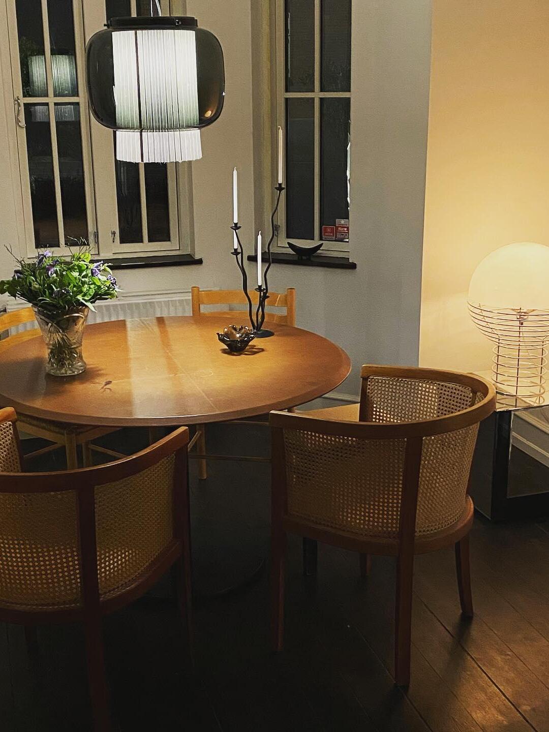 Manila T pendant light over a round dining table at night, with cane-back chairs, candles and a separate globe table lamp