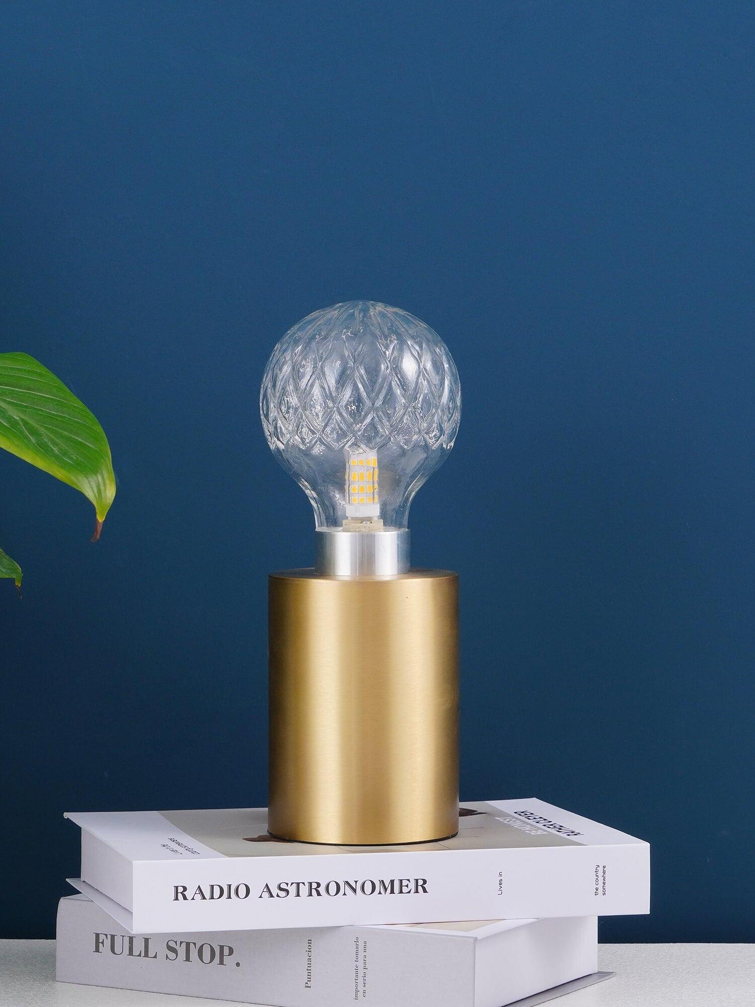 Unlit clear globe table lamp on books against blue wall