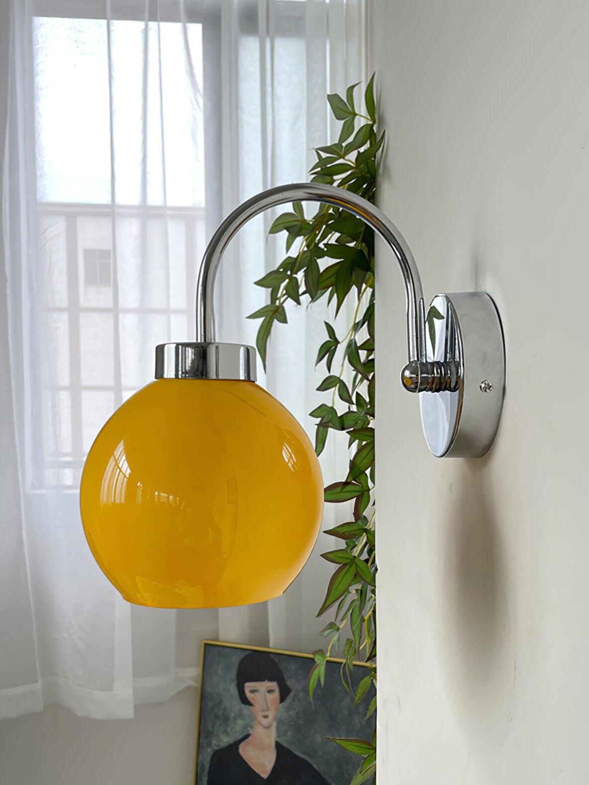 Orange glass globe below arched wall arm near plant and framed portrait