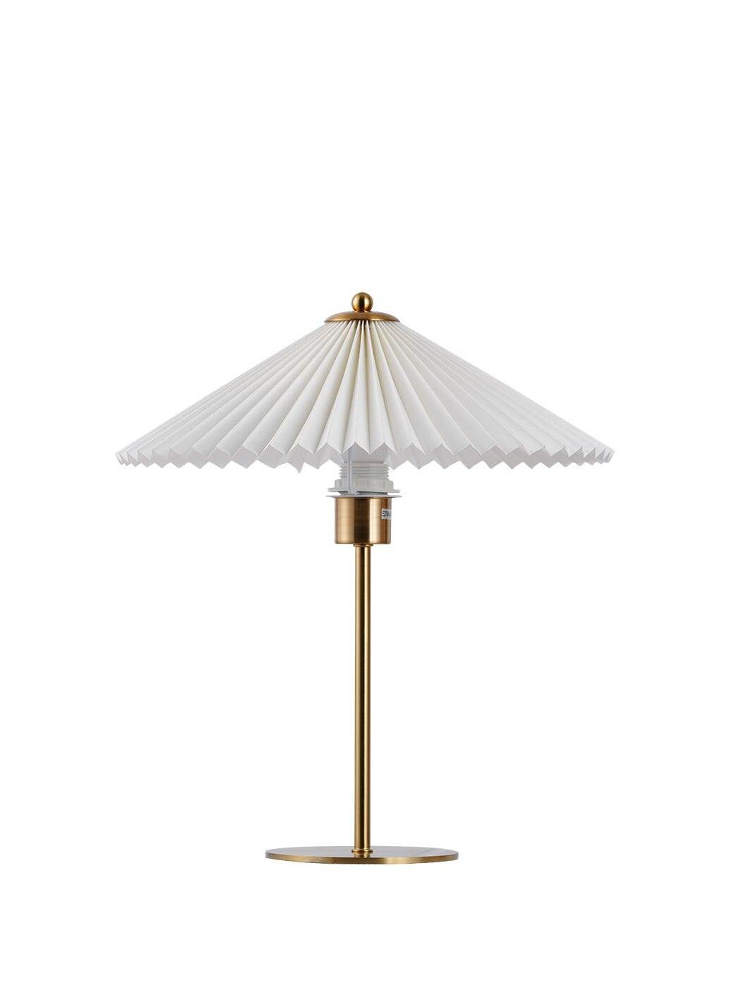 Unlit Perla Gold option on white, with its pale pleated shade, exposed bulb, straight stem and flat round base