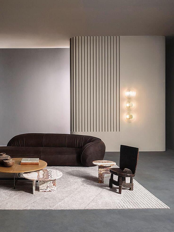 Three round Button wall lights beside a fluted curved wall, above a dark sofa and low tables