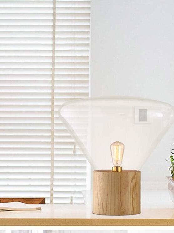 Large clear flared glass lamp with wood base before white window blind
