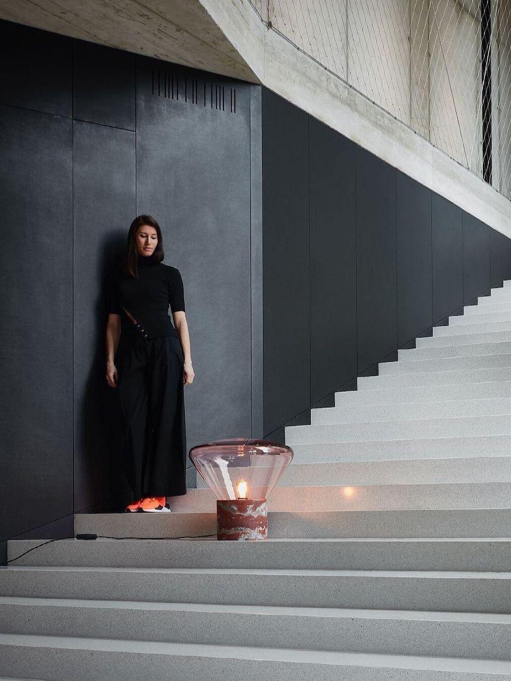 Large pink glass lamp with marbled-looking red base on concrete stairs near person