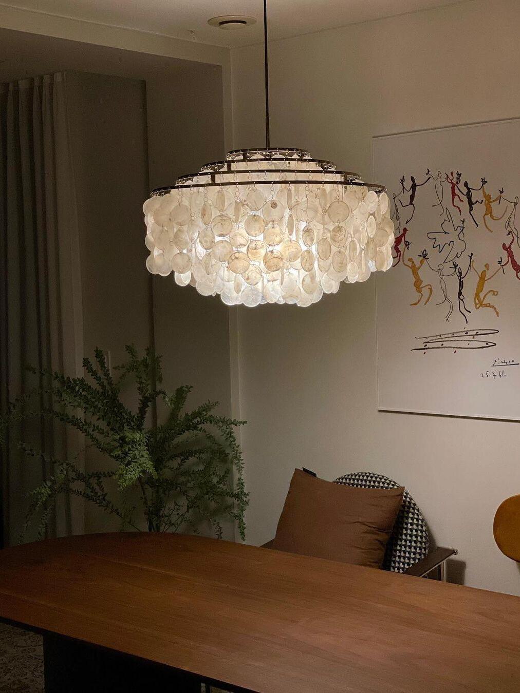 Round shell-disc chandelier above a wooden table beside framed wall art