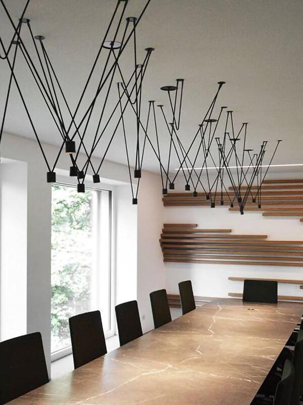 Black geometric pendant arrangement above a long wooden table and black chairs beside windows