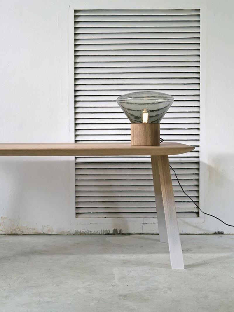 Smoky flared glass lamp on narrow wood bench before window blind