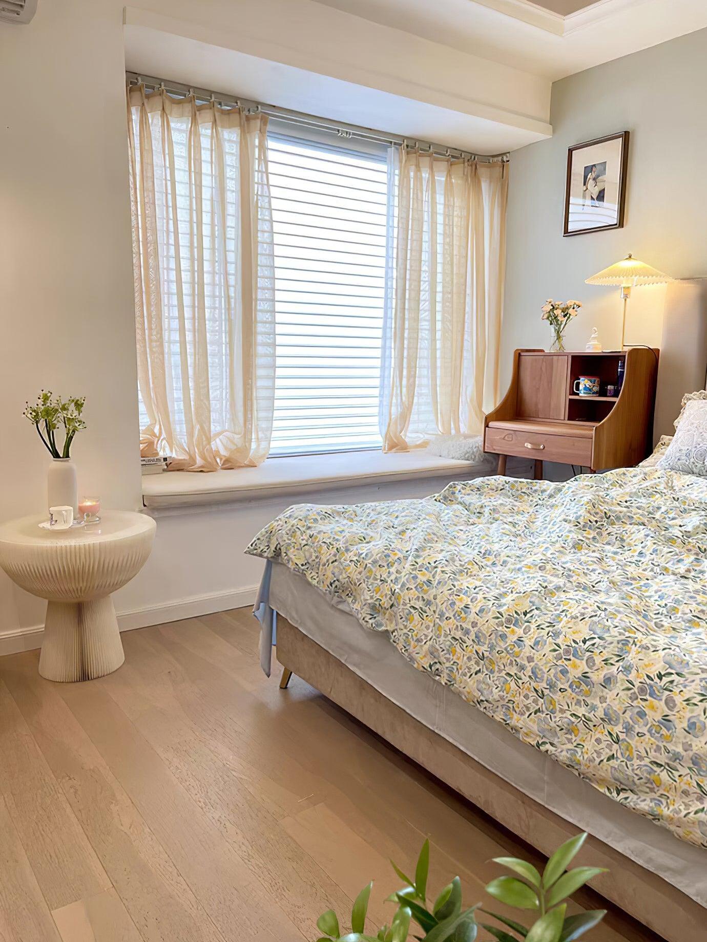 Bedroom view with a small lit table lamp beside the bed, window curtains and patterned bedding