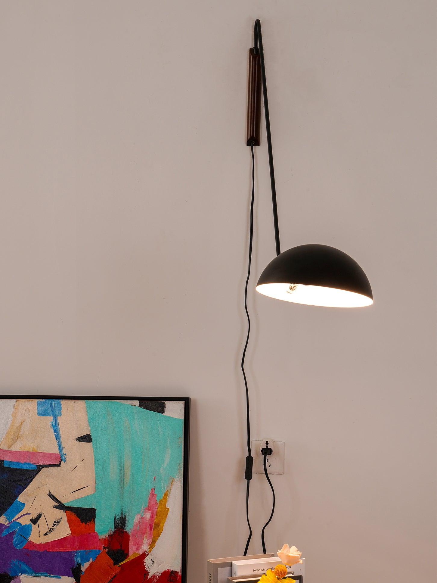 Lit black dome on a steeply angled arm, with dark wooden mount and switched cord above framed art and books