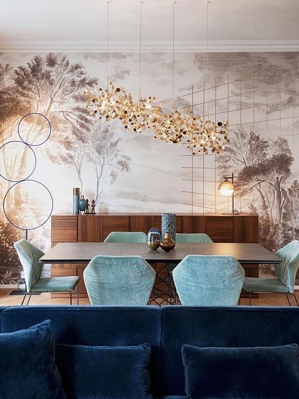 Long gold metal-disc chandelier above a turquoise-chair dining area