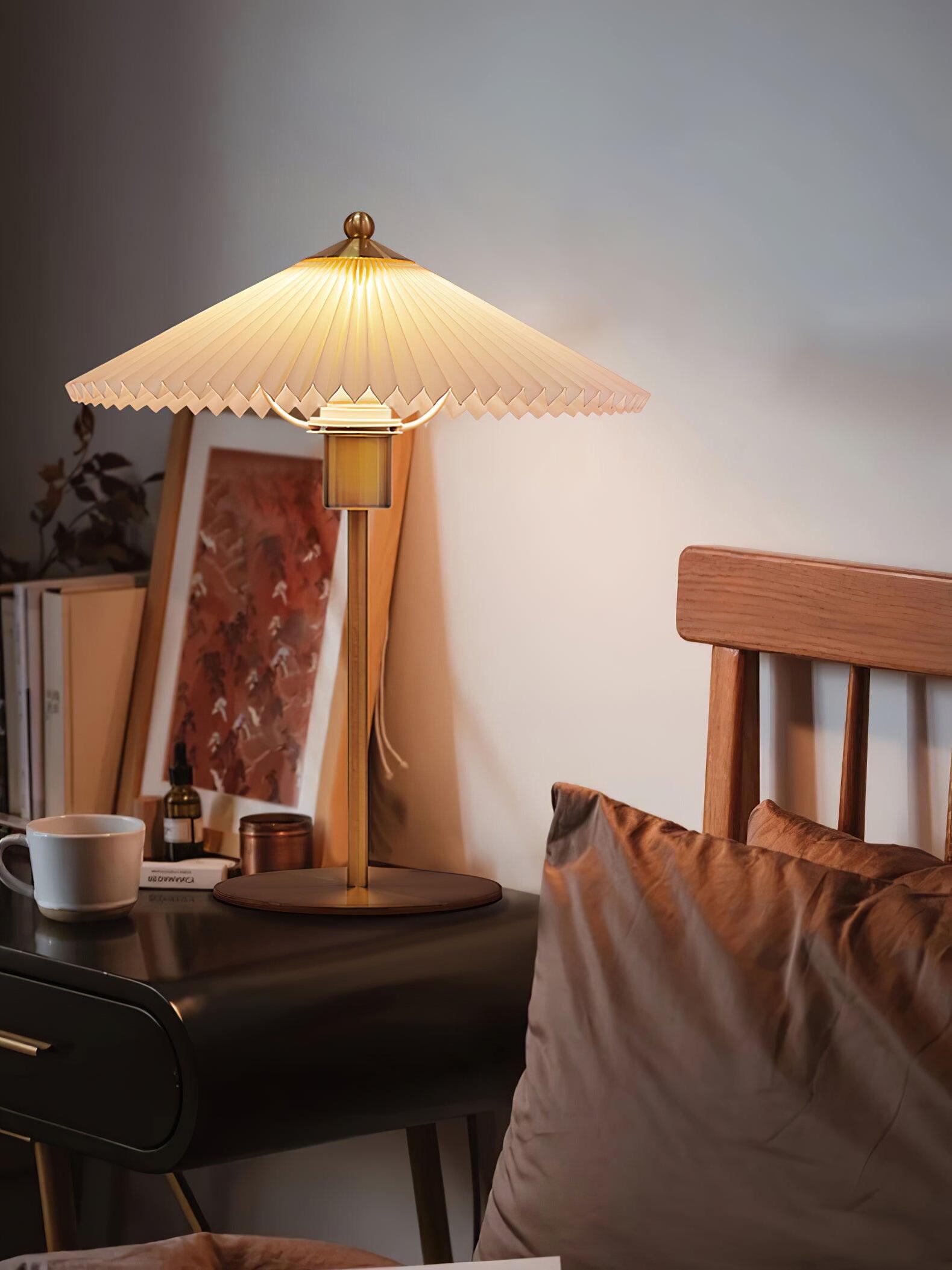 Lit Perla lamp on a bedside surface beside framed art, a wooden headboard and cushions