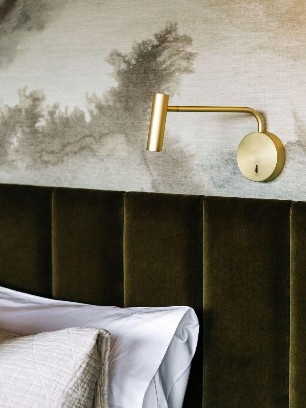 Gold-coloured reading light beside a green headboard