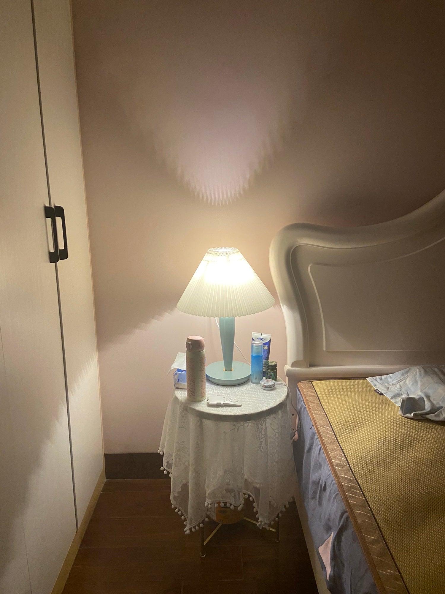 Light-blue table lamp beside bed on round covered table
